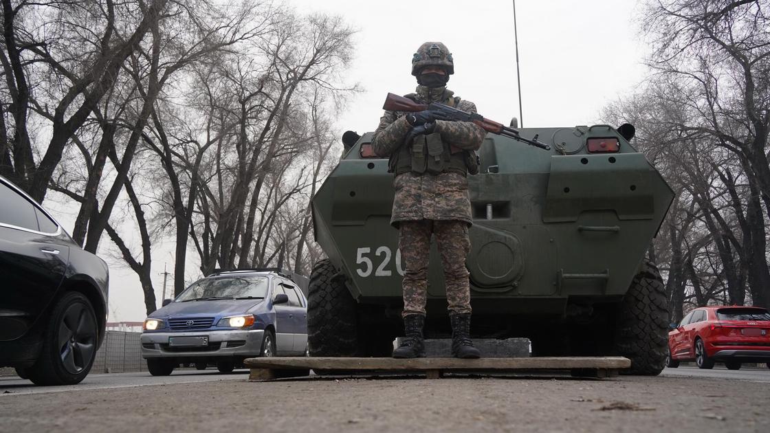 Военнослужащий стоит на блокпосте на фоне БТР