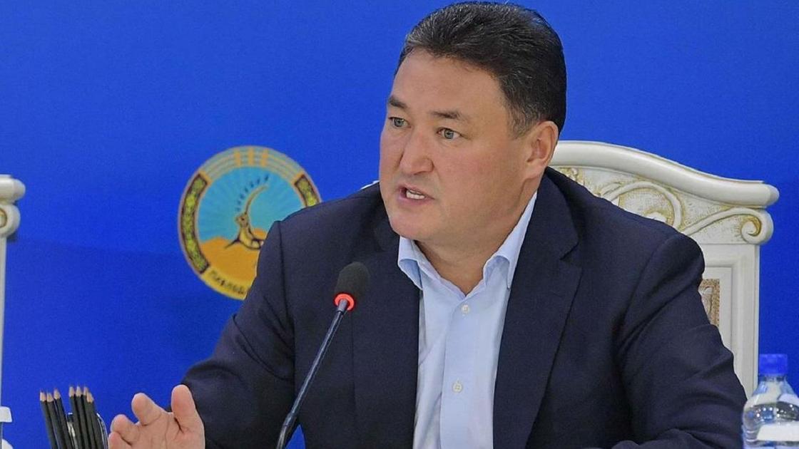 Болат Бакауов сидит за столом на мероприятии