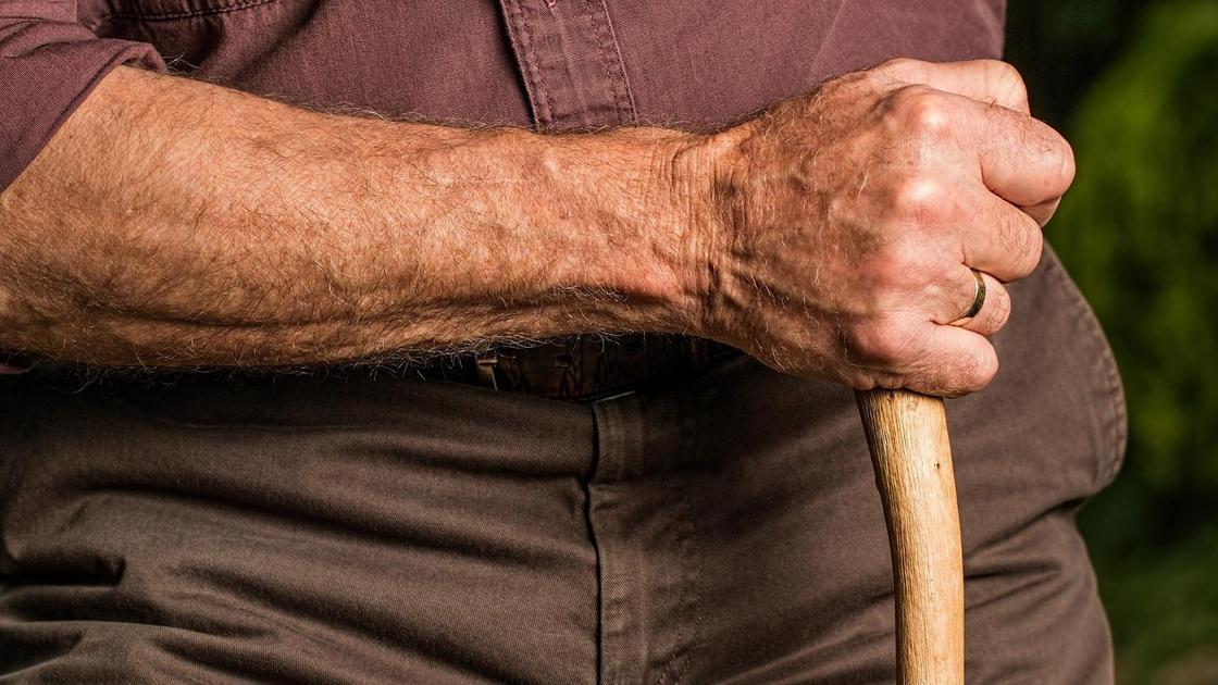 Пожилой мужчина держит в руке трость