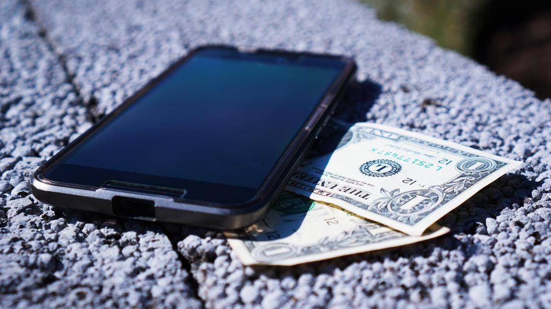 Телефон с деньгам лежат на бетонном бардюре
