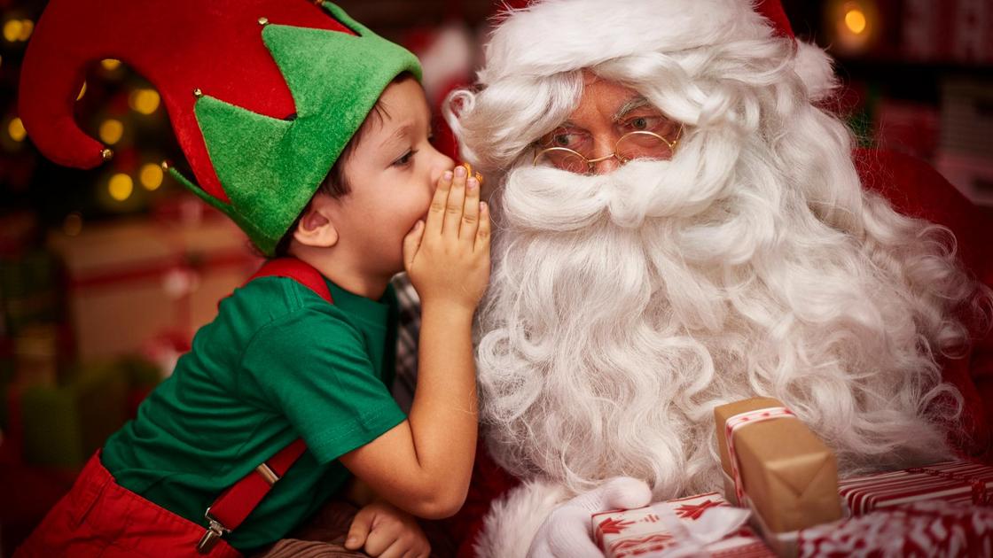 Ребенок в костюме эльфа шепчет на ухо Санта Клаусу