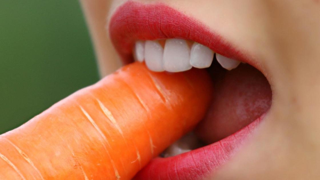 Девушка кусает морковь