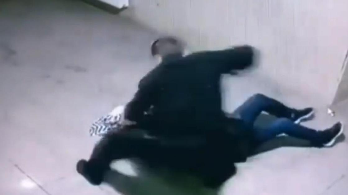 Мужчина наносит удар лежащей на полу женщине