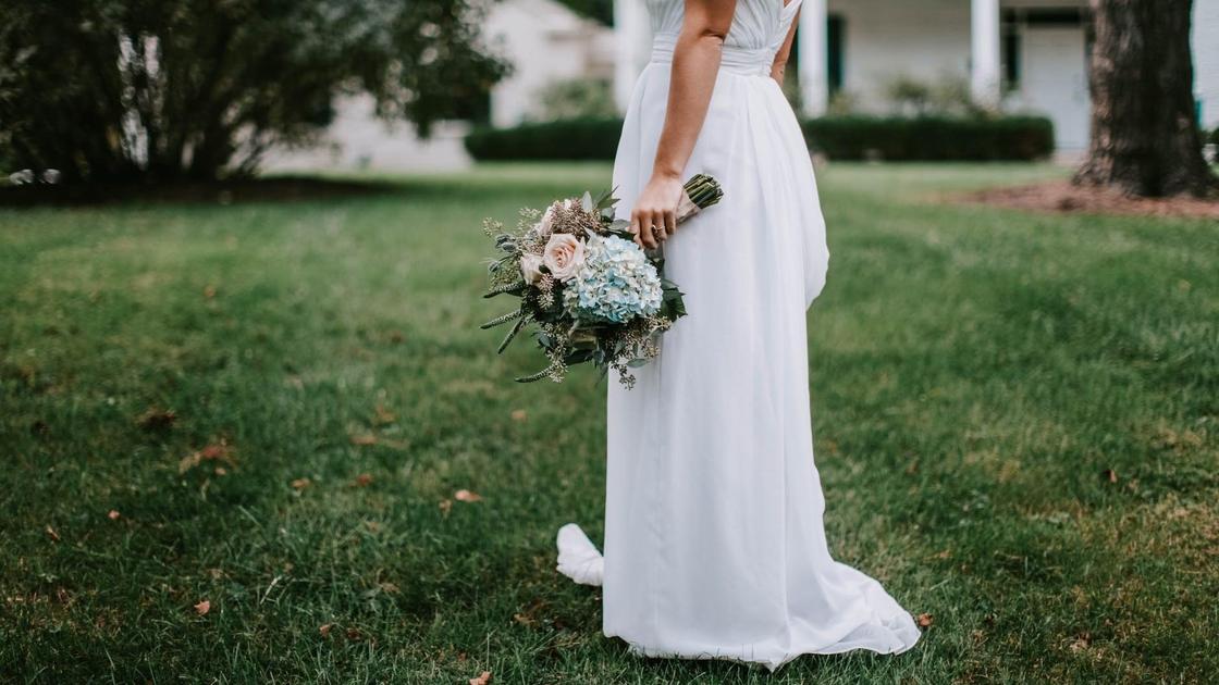 Невеста стоит на газоне в белом платье