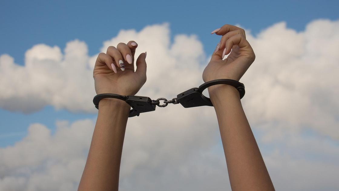 Женские руки в наручниках на фоне неба