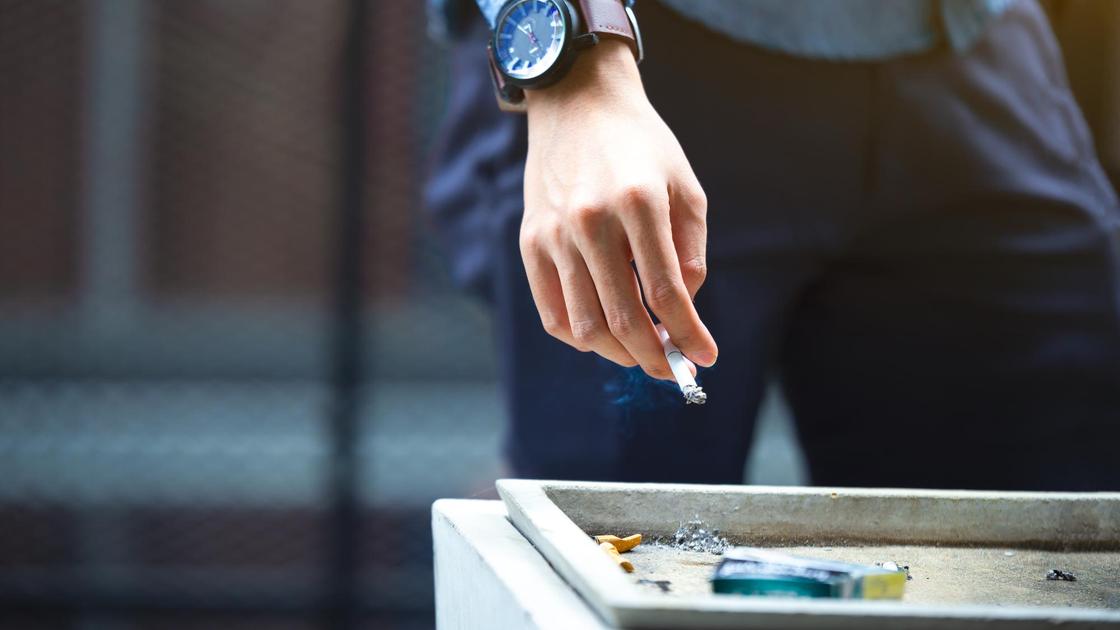 Мужчина выкидывает окурок от сигареты в мусорку