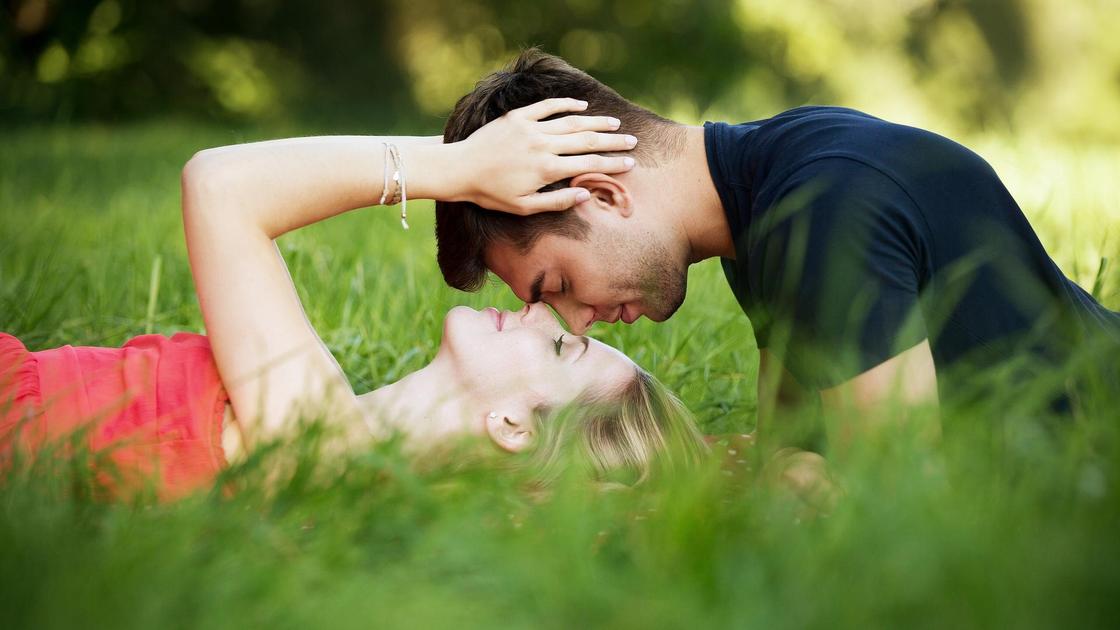 Парень и девушка лежат на траве, соприкасаясь лицами