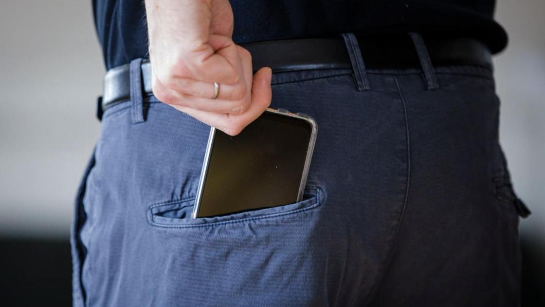 Мужчина достает телефон из заднего кармана брюк