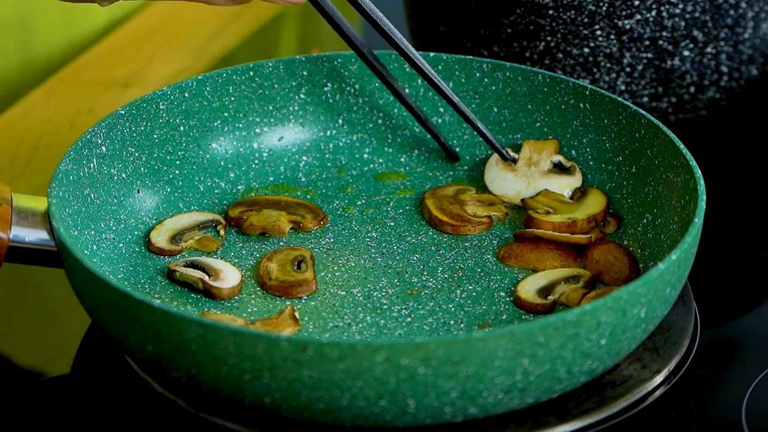 Палочками переворачивают грибы шампиньоны на сковороде