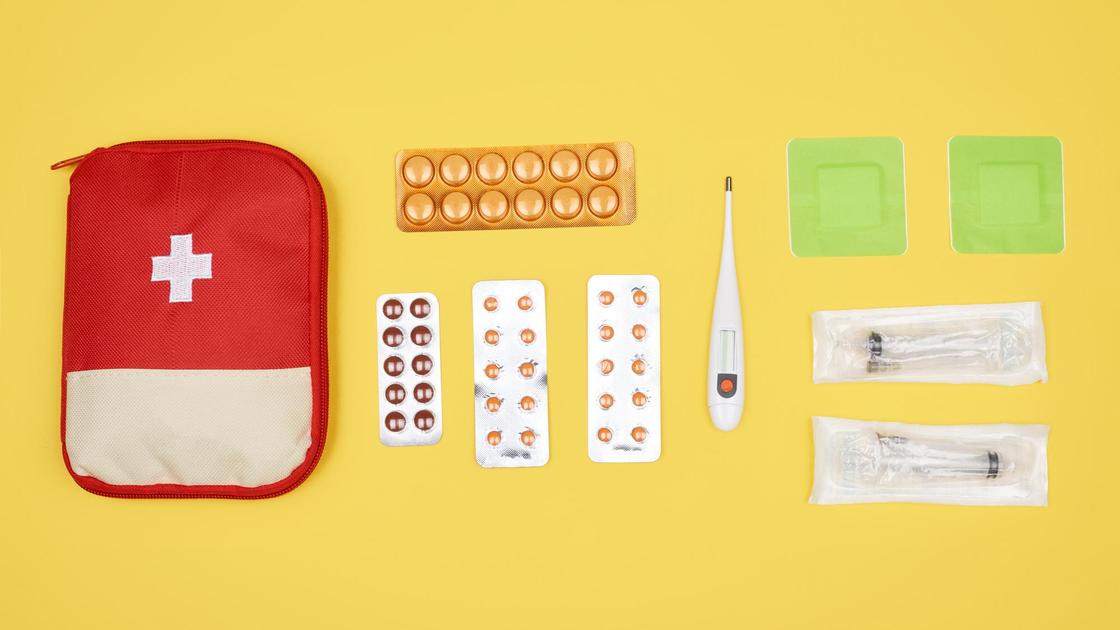 Аптечка, таблетки, термометр, шприцы на желтом фоне