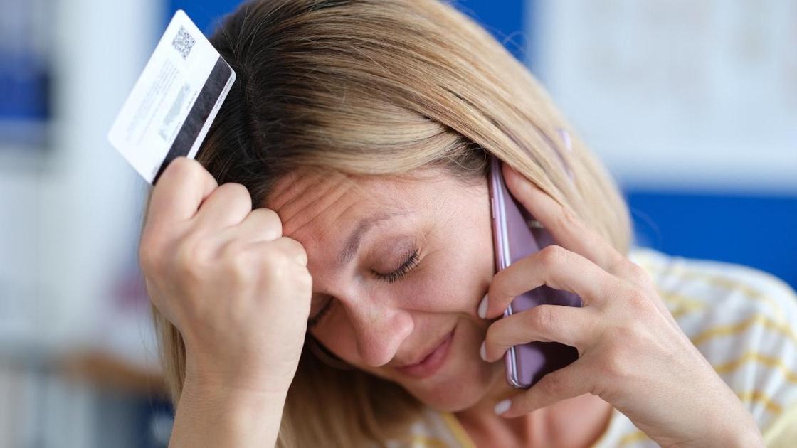 Женщина беседует по телефону и держит в руках банковскую карту