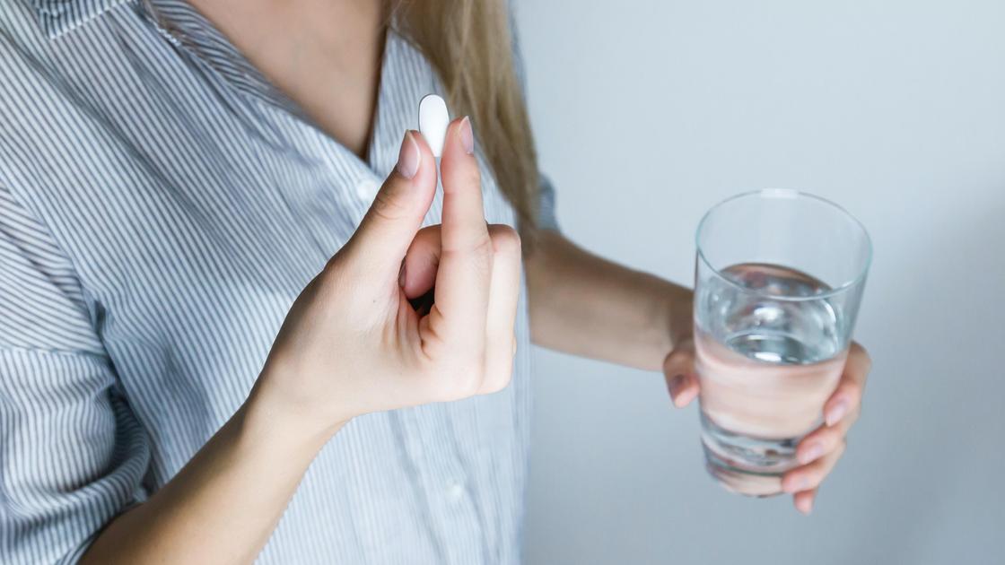 Женщина держит лекарство и стакан с водой