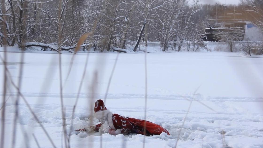 Мужчина в костюме Деда Мороза лежит на льду
