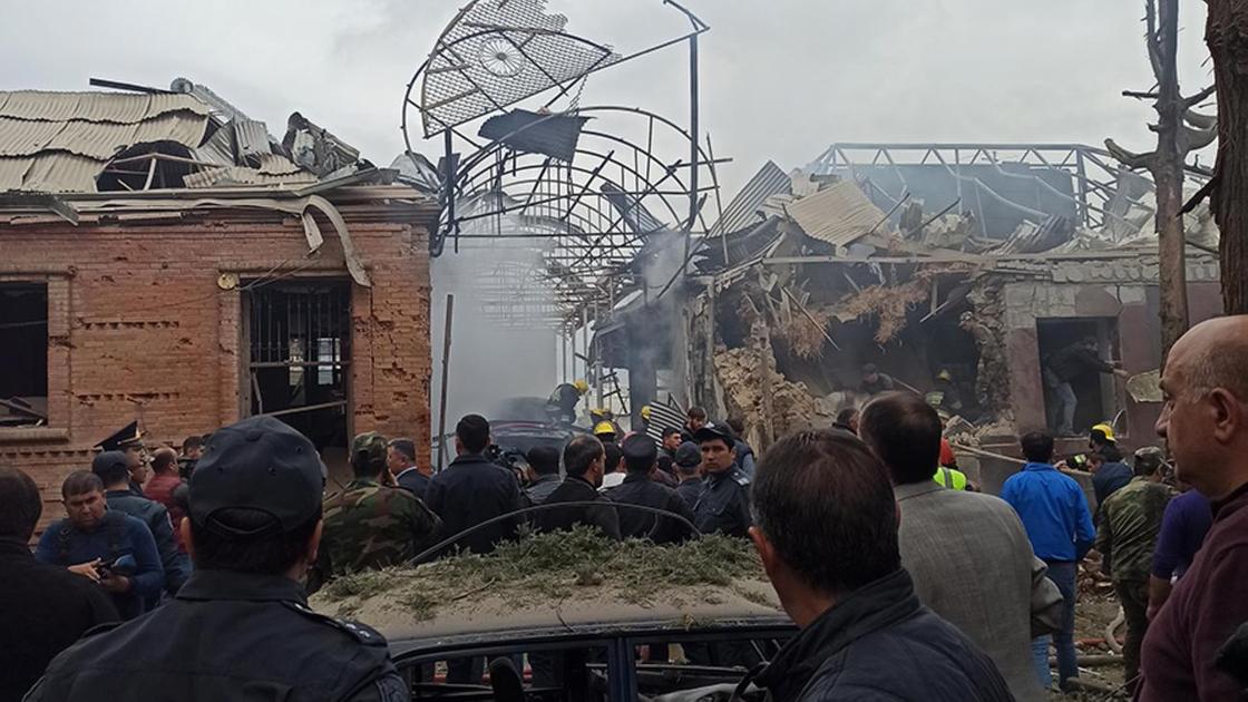 Люди стоят возле поврежденных зданий в Гяндже