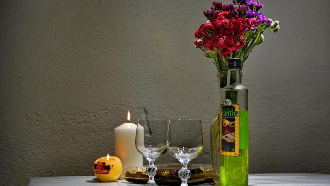 На столе бутылка абсента, бокалы, свечи и цветы