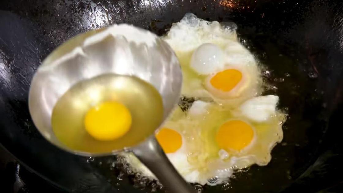 Разбитые яйца переносятся на сковороду в половнике