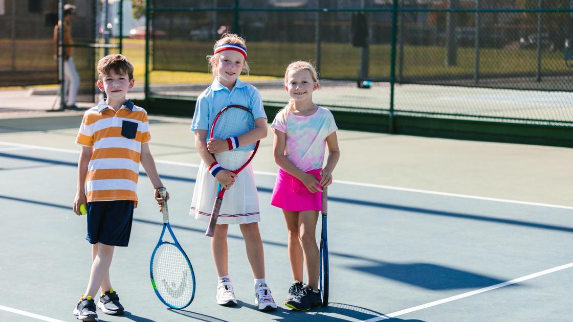 Девочки и мальчик стоят с ракетками для тенниса