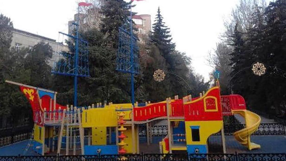 Детская площадка на фоне елей в Алматы