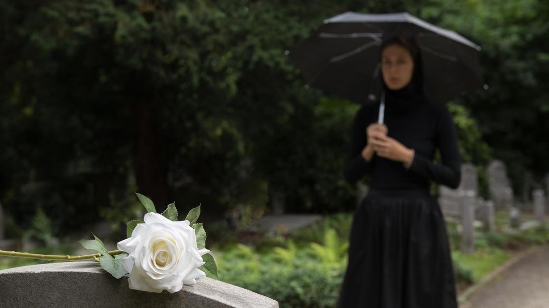 Женщина стоит под зонтом перед могилой