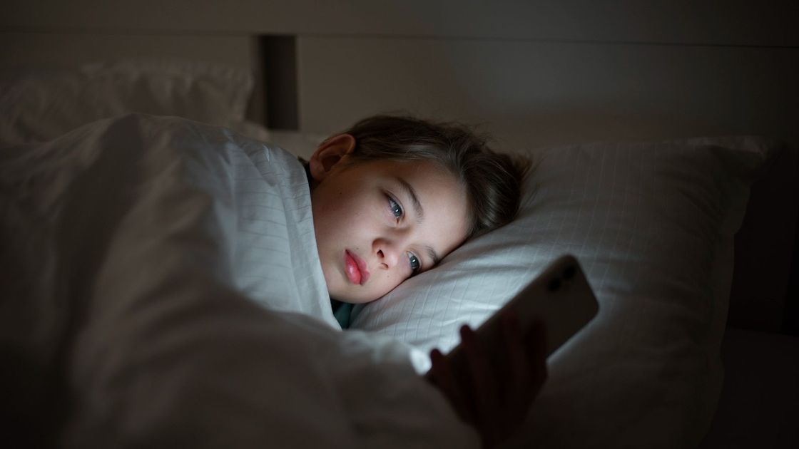 Мальчик смотрит в телефон, лежа в постели