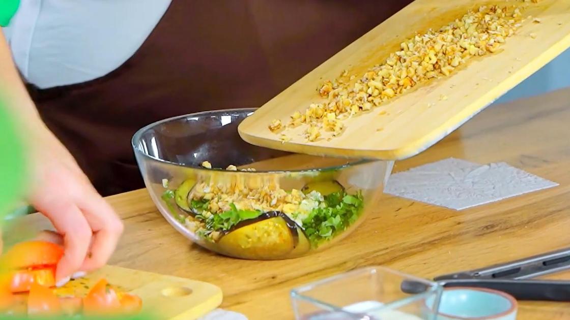 В салатник с баклажанами и зеленью насыпают орехи с разделочной доски