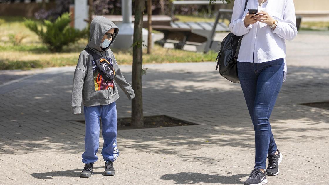 Ребенок в маске идет по улице с мамой