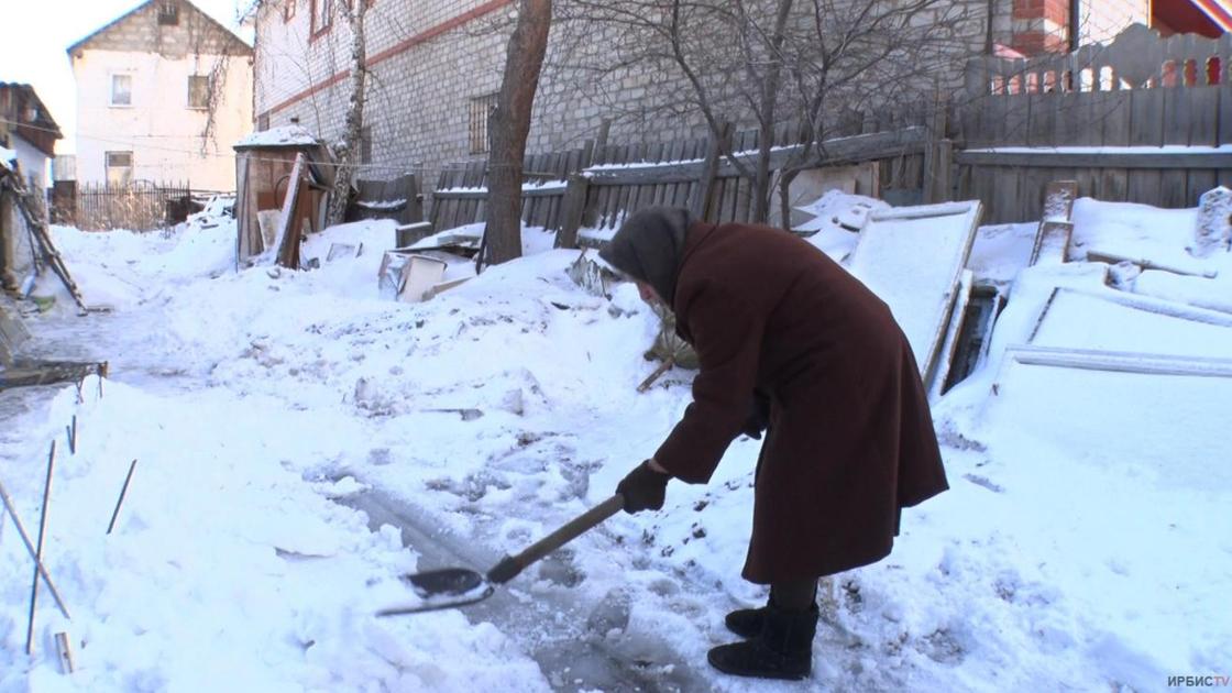 Пожилая женщина убирает снег лопатой