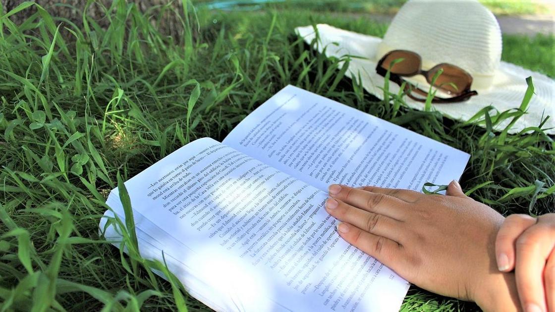 Открытая книга на траве и женские руки