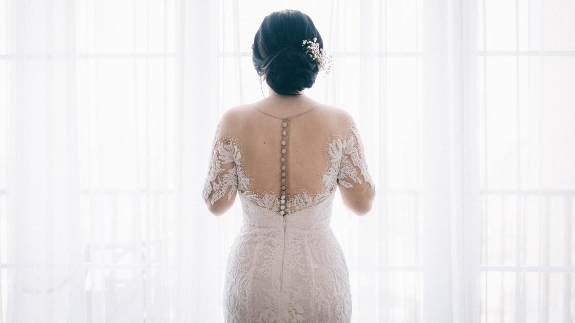 Невеста в свадебном платье стоит у окна