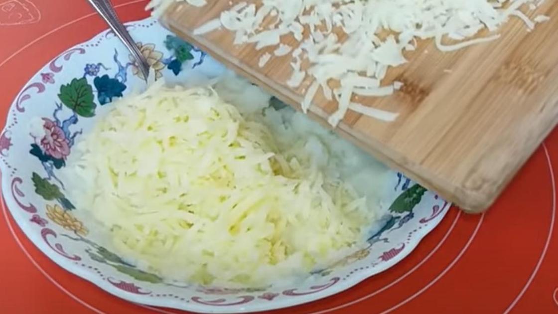 В миску с картофелем засыпают с деревянной дощечки натертый сыр