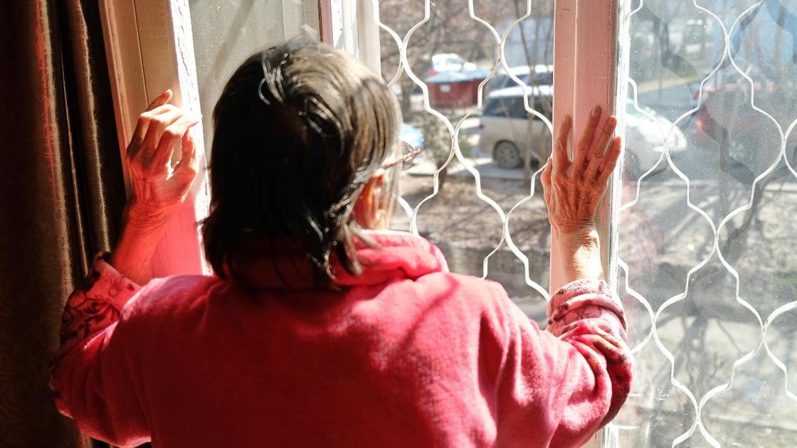 Пожилая женщина стоит возле окна