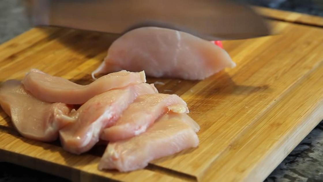 Куриное филе нарезают ножом на разделочной доске