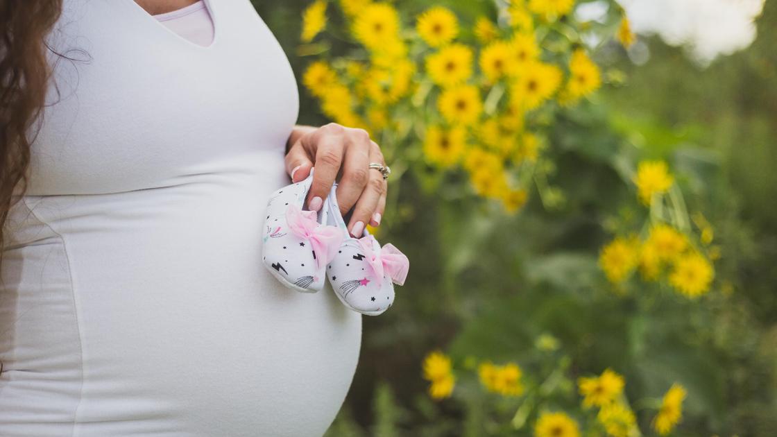 Беременная женщина держит детские тапочки на животе