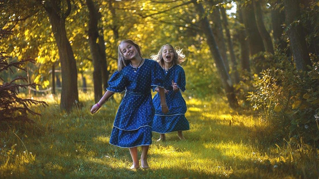 Девочки-близняшки бегут в синих платьях по роще