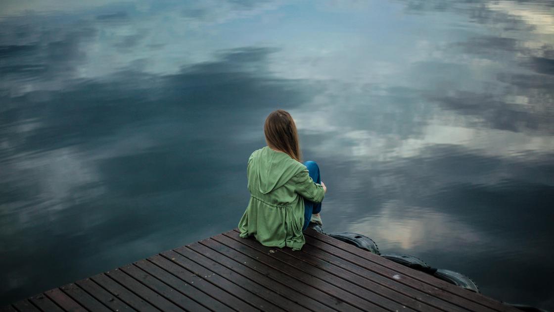 Девушка сидит на пирсе у водоема