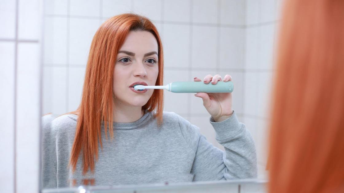 Девушка чистит зубы у зеркала