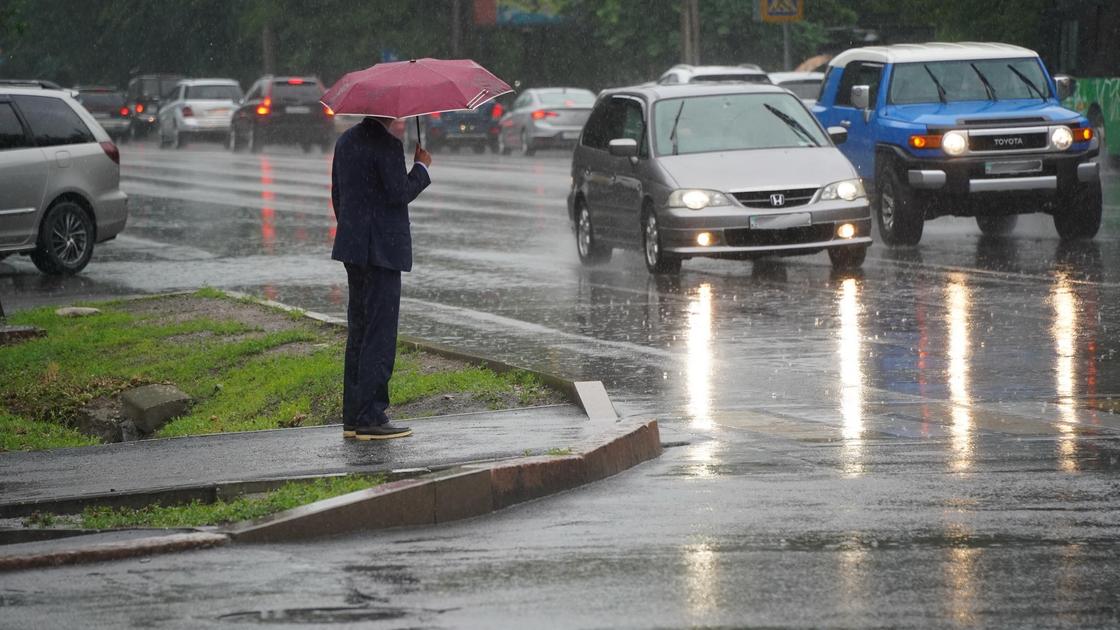 Человек с зонтом стоит у дороги