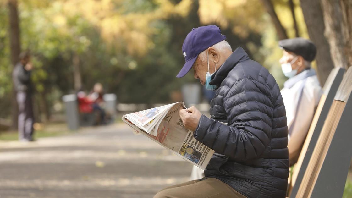 Мужчина читает газету, сидя на скамейке
