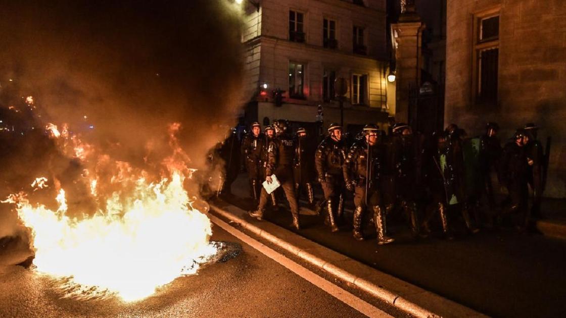 Французские полицейские идут мимо горящего мусора