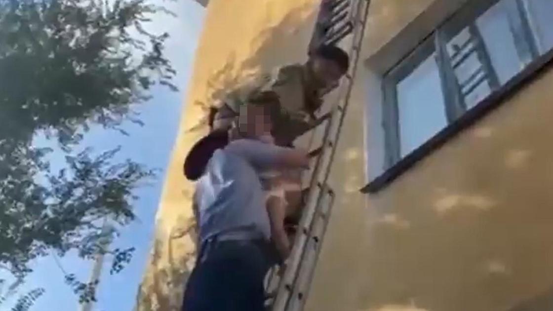 Спасатель передает ребенка полицейскому на лестнице
