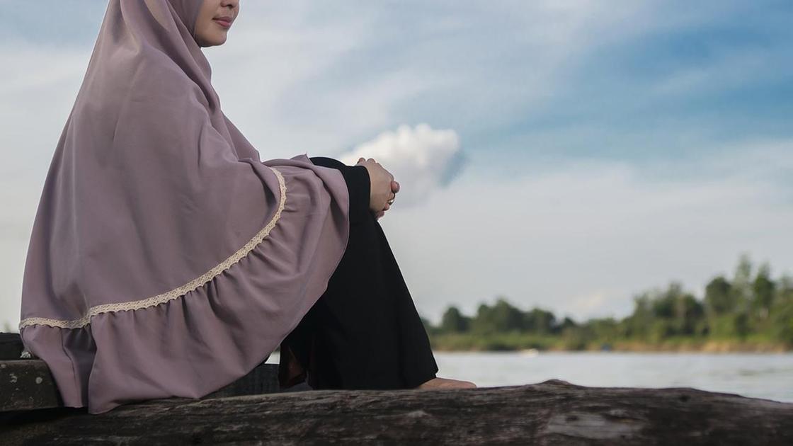 Девушка в хиджабе сидит у воды