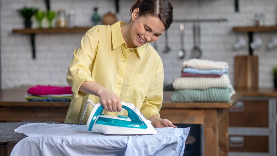 Женщина гладит утюгом светлую рубашку на гладильной доске