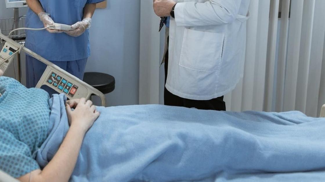 Женщина лежит на больничной койке, рядом стоят врачи