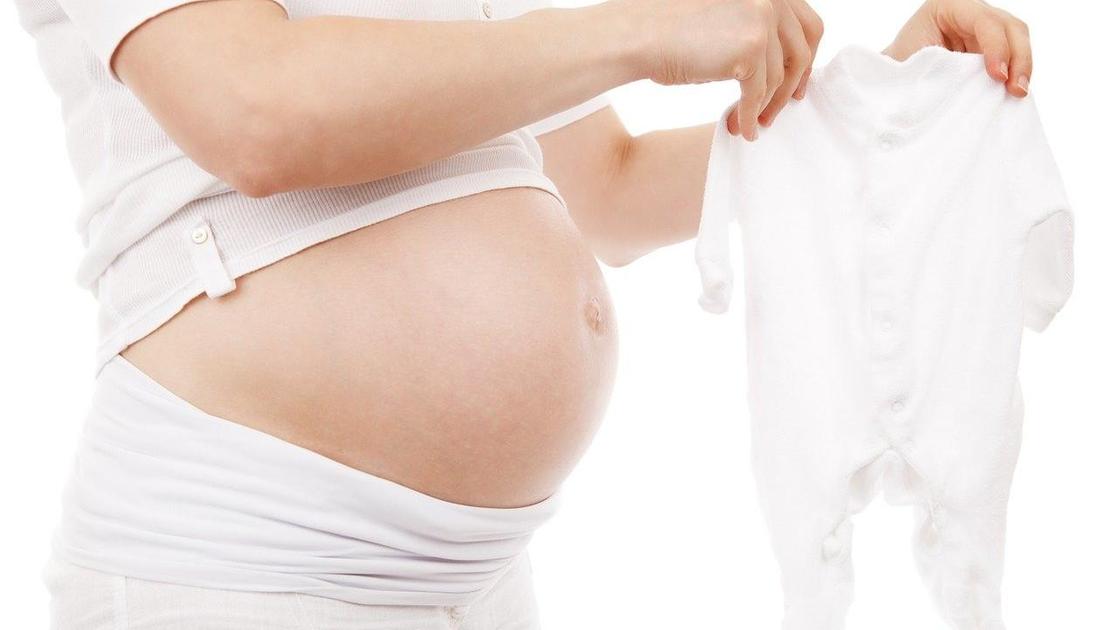 Беременная женщина с оголенным животом держит слип для ребенка