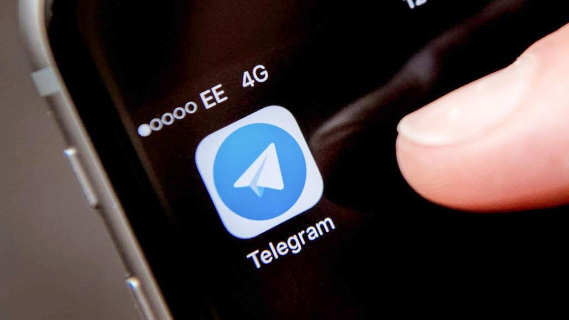 Человек нажимает пальцем руки на иконку приложения Telegram