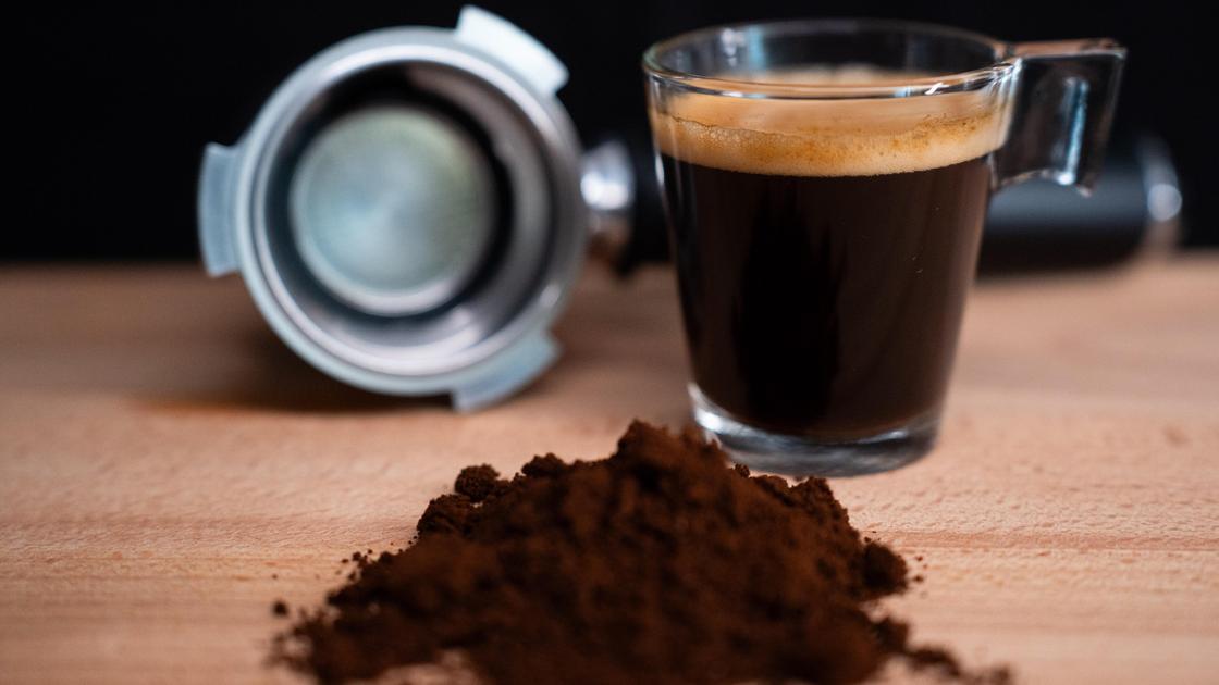 Чашка кофе стоит на столе рядом с молотыми зернами