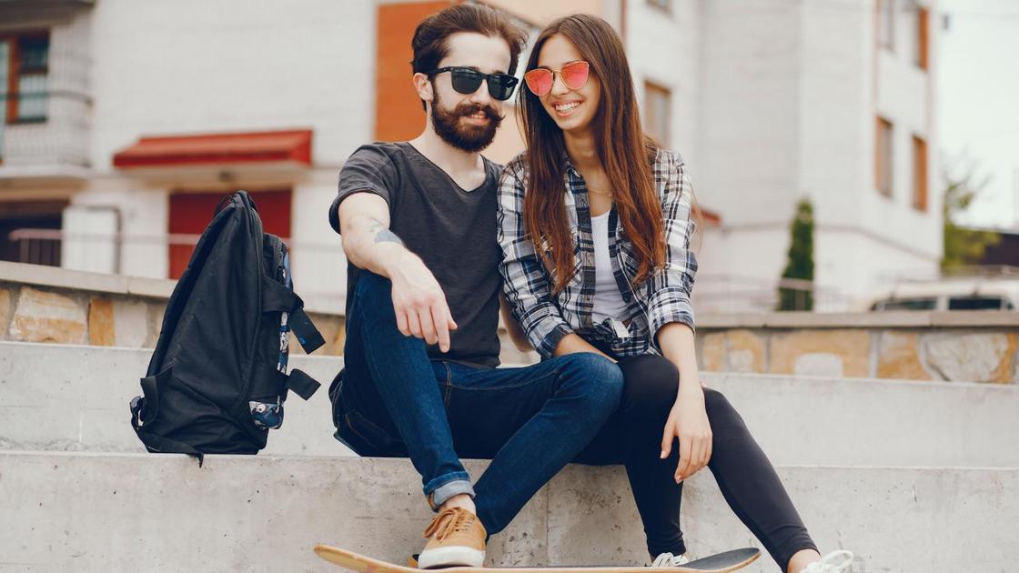 Мужчина с бородой и девушка в рубашке в клетку со скейтом и рюкзаком