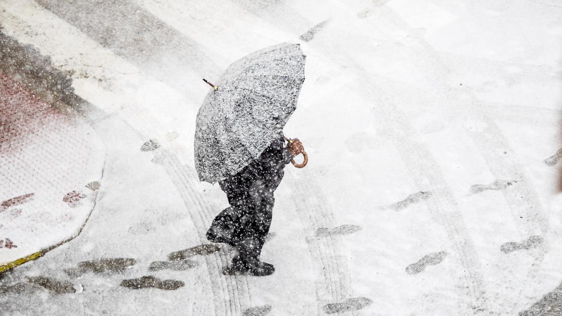 Человек переходит дорогу под зонтом во время снегопада