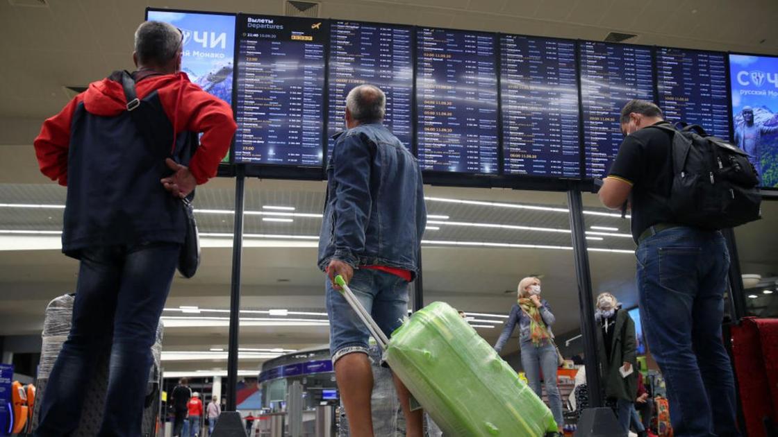 Авиапассажиры с багажом смотрят на табло
