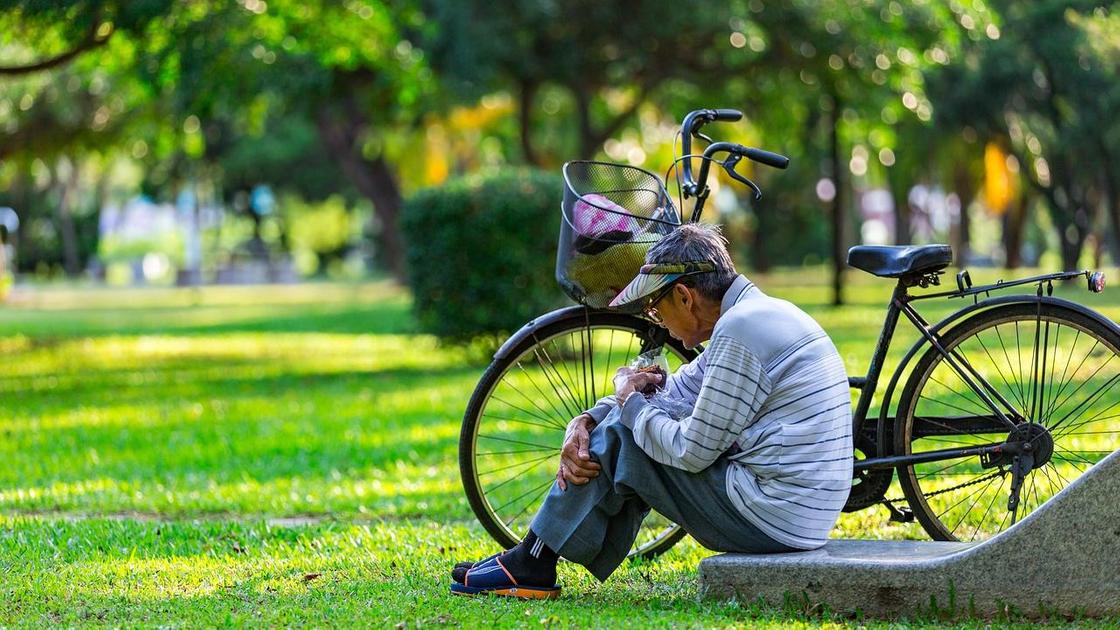 Мужчина сидит в парке рядом с велосипедом